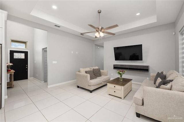 living room with a tray ceiling, light tile patterned flooring, and baseboards