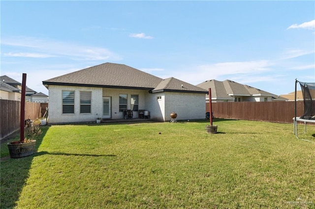 back of property with a fenced backyard, a trampoline, a lawn, and brick siding