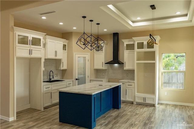 kitchen featuring white cabinetry, sink, wall chimney exhaust hood, hanging light fixtures, and a kitchen island