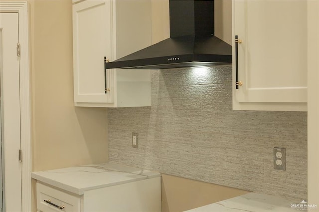 kitchen with tasteful backsplash, light stone counters, white cabinets, and wall chimney range hood