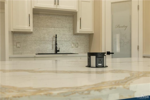 kitchen with backsplash, white cabinets, light stone countertops, and sink