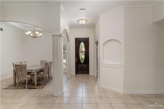 foyer entrance featuring a notable chandelier, ornate columns, crown molding, and light tile patterned floors