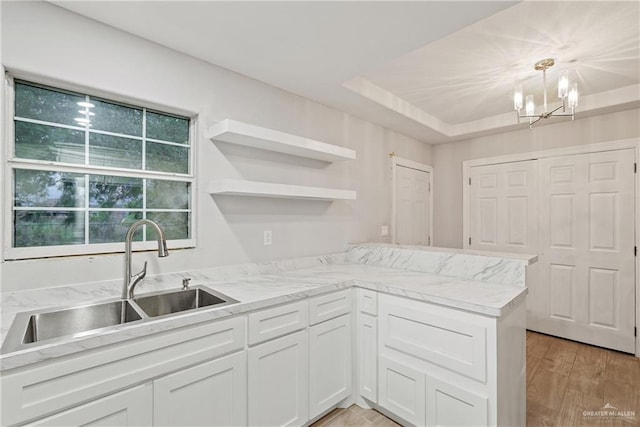 kitchen with white cabinetry, a tray ceiling, an inviting chandelier, a sink, and light wood finished floors