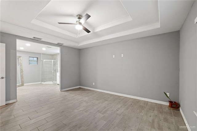 spare room with baseboards, light wood-type flooring, ceiling fan, and a raised ceiling