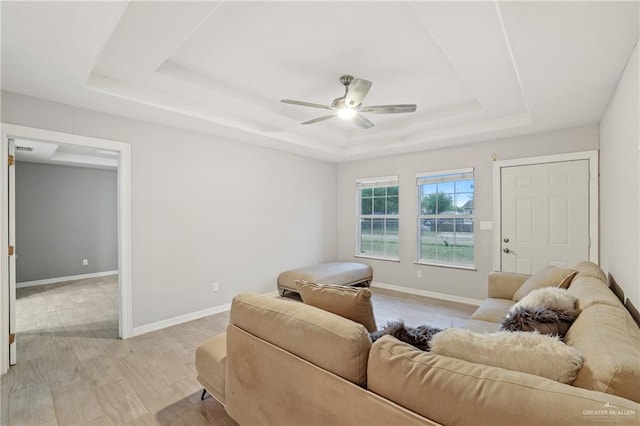 living room featuring a tray ceiling, baseboards, light wood-style floors, and ceiling fan