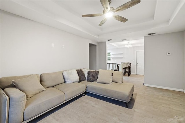 living room with light wood-style flooring, a tray ceiling, visible vents, and ceiling fan