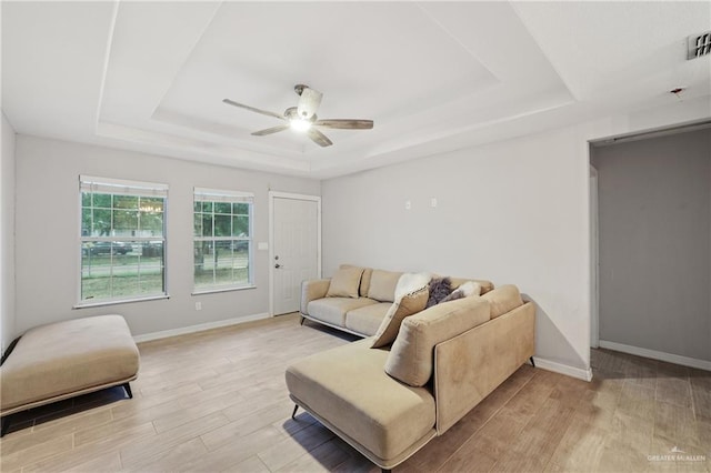 living area featuring ceiling fan, light wood-type flooring, and a raised ceiling