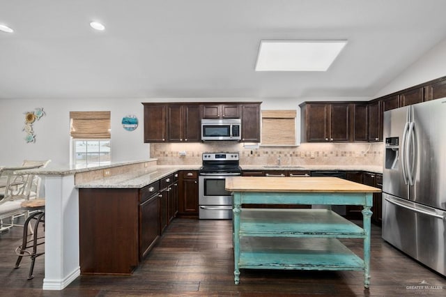 kitchen with light stone countertops, dark brown cabinets, stainless steel appliances, and a kitchen bar