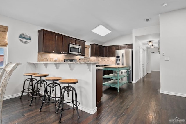 kitchen featuring dark hardwood / wood-style flooring, dark brown cabinets, stainless steel appliances, and a breakfast bar area