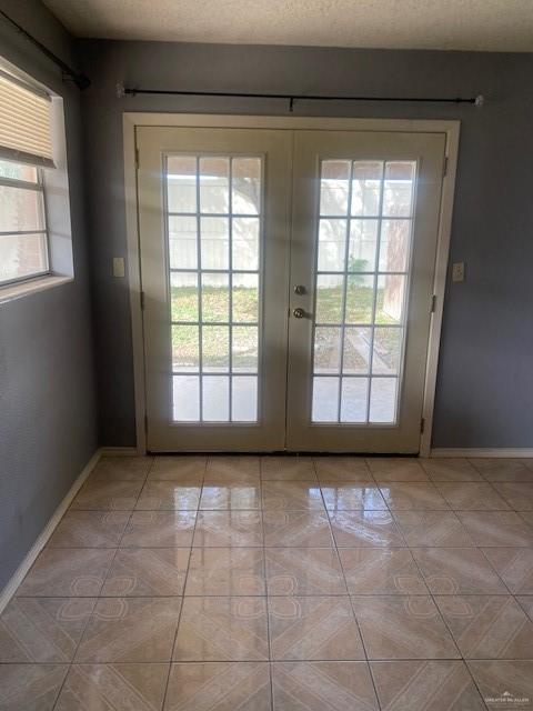 doorway to outside with french doors, a textured ceiling, light tile patterned floors, and plenty of natural light