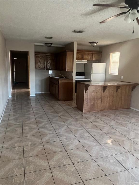 kitchen with kitchen peninsula, a textured ceiling, a breakfast bar, and white fridge