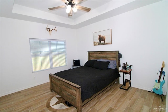 bedroom with light wood-type flooring, a tray ceiling, and ceiling fan