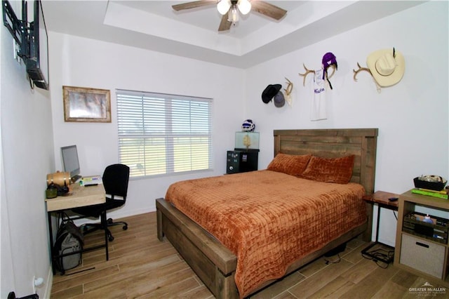 bedroom with a raised ceiling, ceiling fan, and wood-type flooring