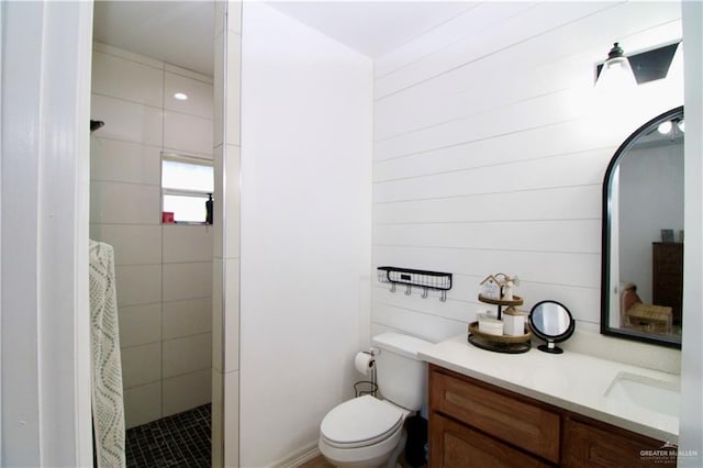 bathroom with a tile shower, wooden walls, vanity, and toilet