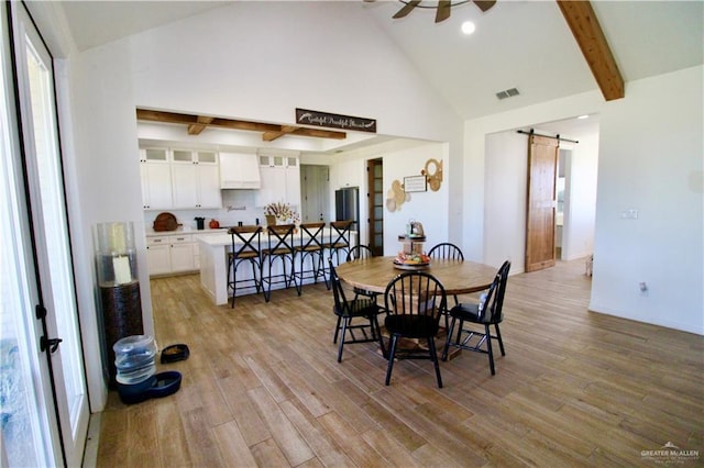 dining room featuring beam ceiling, ceiling fan, a barn door, light hardwood / wood-style flooring, and high vaulted ceiling