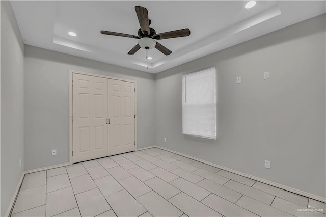 unfurnished bedroom featuring a tray ceiling, ceiling fan, and a closet