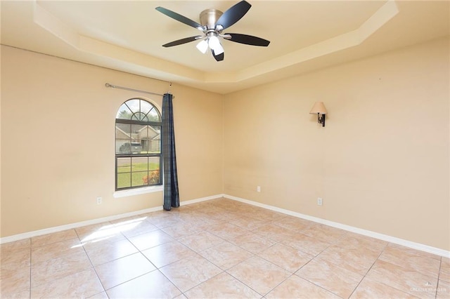 tiled empty room featuring a tray ceiling and ceiling fan