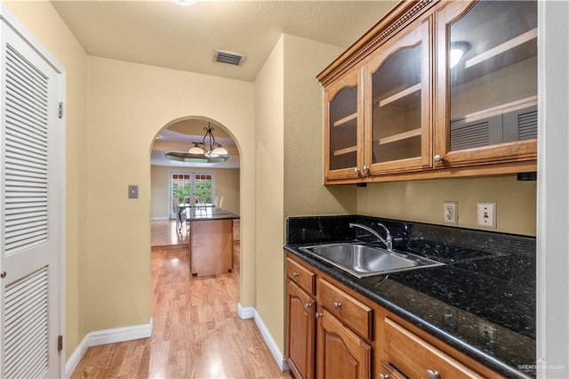 3206 Marion Ct, Harlingen, TX 78550 - kitchen with light wood-type flooring, glass insert cabinets, arched walkways, brown cabinets, and dark stone counters