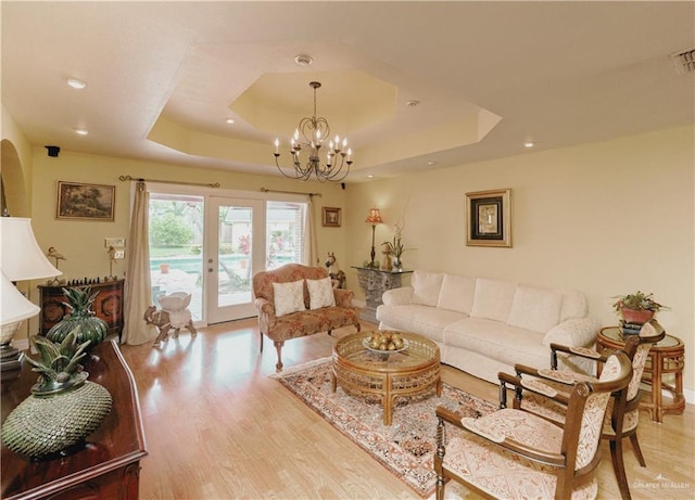 living room with light wood-type flooring, french doors, an inviting chandelier, and a raised ceiling