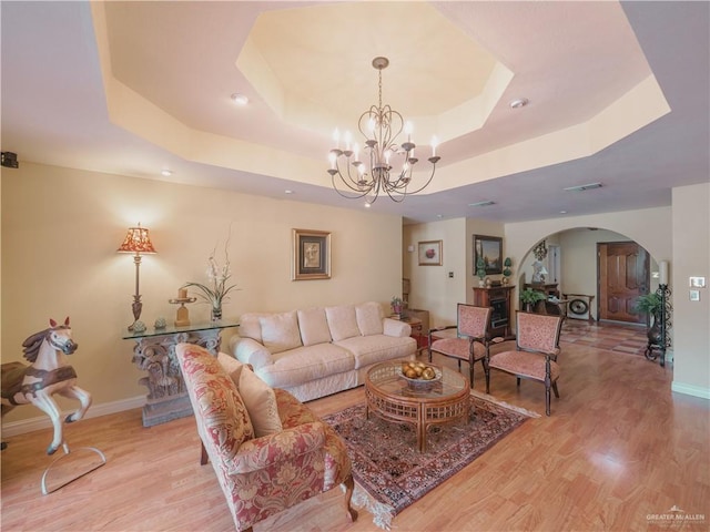 living room featuring a raised ceiling, light wood-type flooring, and a notable chandelier