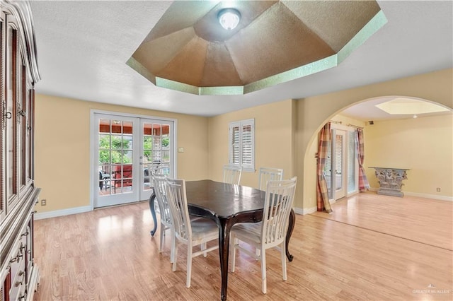 3206 Marion Ct, Harlingen, TX 78550 - dining area featuring arched walkways, french doors, light wood-style floors, a tray ceiling, and a textured ceiling