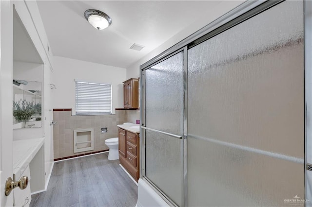 1702 Elmwood Dr, Harlingen, TX 78550 - bathroom featuring tile walls, vanity, toilet, wood finished floors, and a shower with door