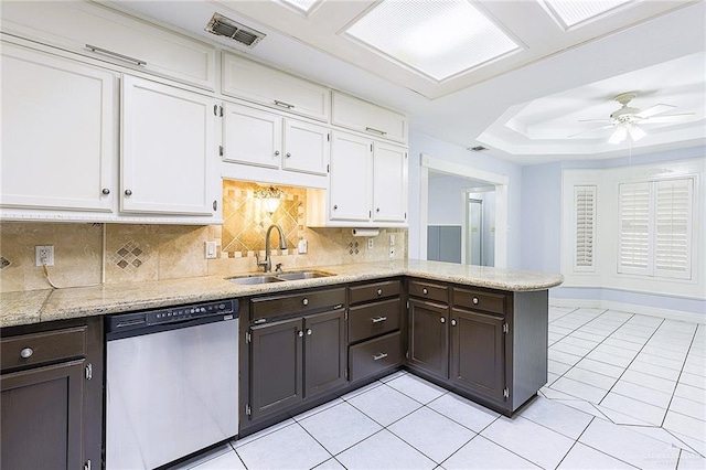 kitchen featuring tasteful backsplash, sink, white cabinets, stainless steel dishwasher, and a tray ceiling