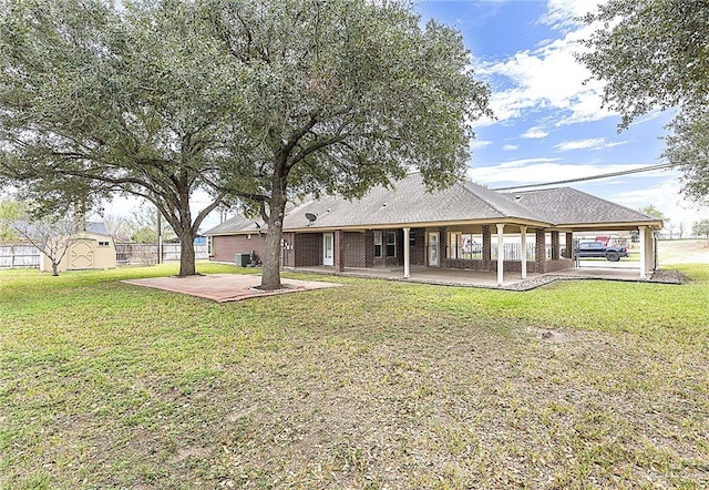 rear view of property featuring a storage unit, a yard, and a patio area