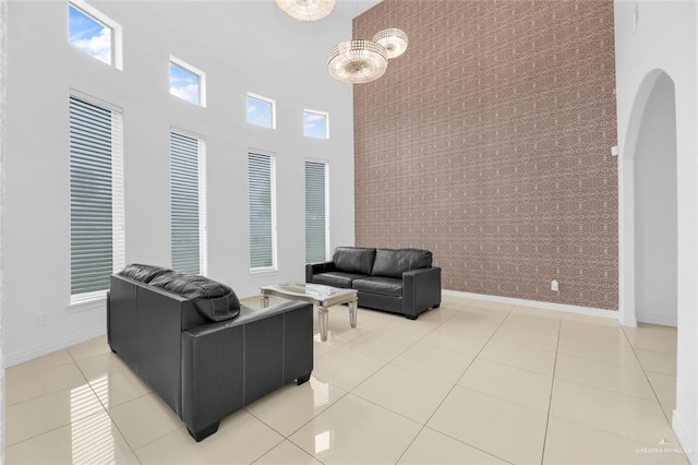 living area featuring light tile patterned floors, baseboards, a towering ceiling, and arched walkways