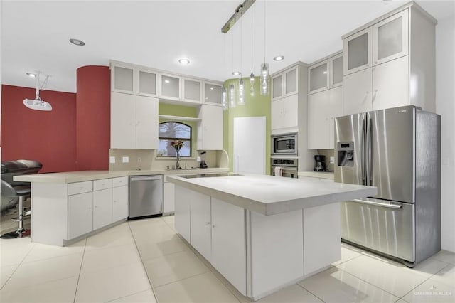 kitchen with light countertops, stainless steel appliances, pendant lighting, and glass insert cabinets