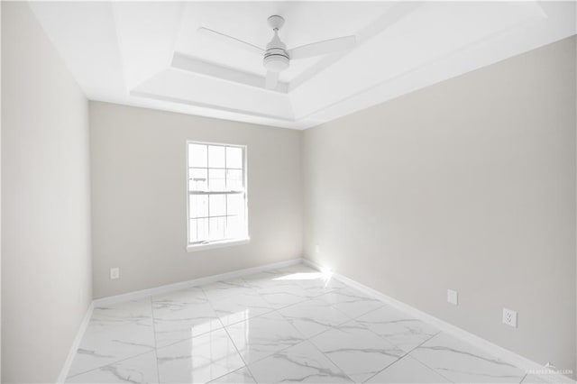 empty room with ceiling fan and a tray ceiling