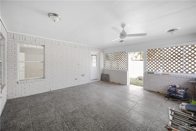 empty room featuring ceiling fan and brick wall