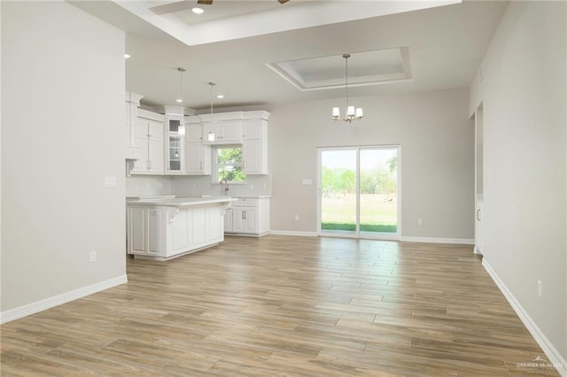 unfurnished living room with baseboards, a raised ceiling, and light wood-style flooring