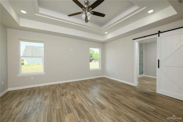 unfurnished room featuring a raised ceiling, a barn door, and wood finished floors