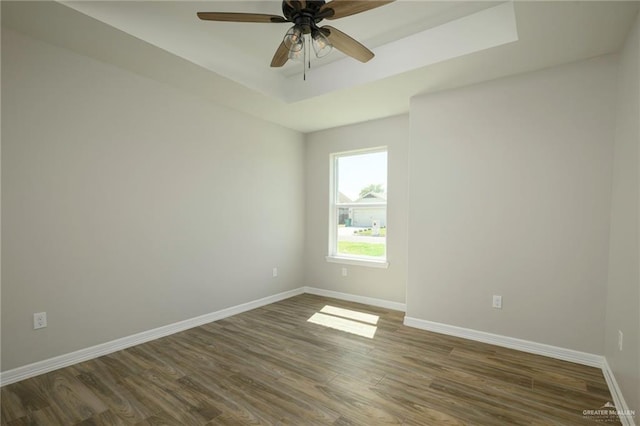 empty room with dark wood finished floors, a tray ceiling, a ceiling fan, and baseboards