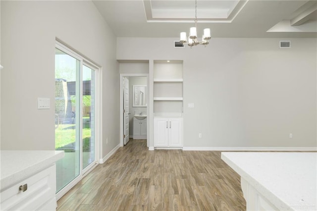 unfurnished dining area featuring baseboards, visible vents, light wood-style flooring, a raised ceiling, and a chandelier