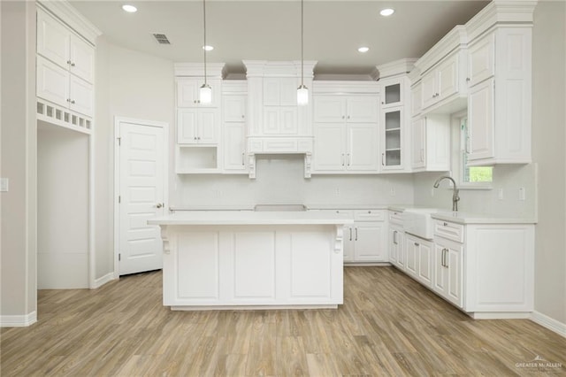 kitchen featuring light wood finished floors, a sink, light countertops, white cabinetry, and a center island