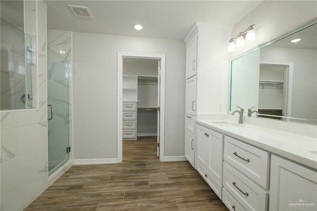 bathroom featuring a walk in closet, wood finished floors, visible vents, and a stall shower