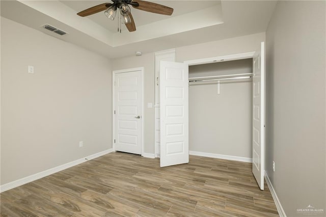 unfurnished bedroom with visible vents, a raised ceiling, baseboards, and wood finished floors