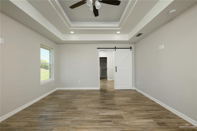 empty room featuring a barn door, a raised ceiling, baseboards, and wood finished floors