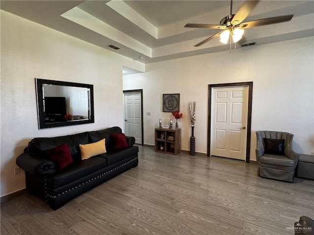 living room featuring a raised ceiling, ceiling fan, and wood-type flooring