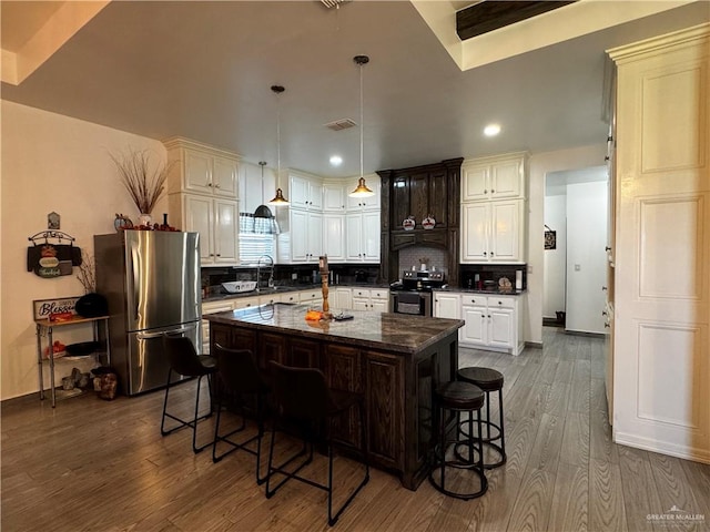 kitchen featuring a kitchen breakfast bar, decorative backsplash, a kitchen island, wood-type flooring, and stainless steel appliances