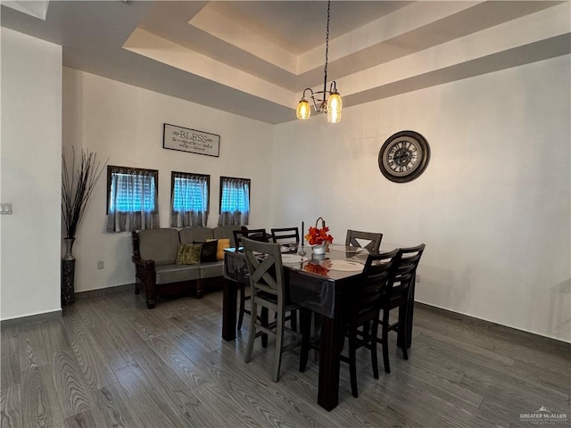 dining area featuring a raised ceiling, dark hardwood / wood-style flooring, and an inviting chandelier