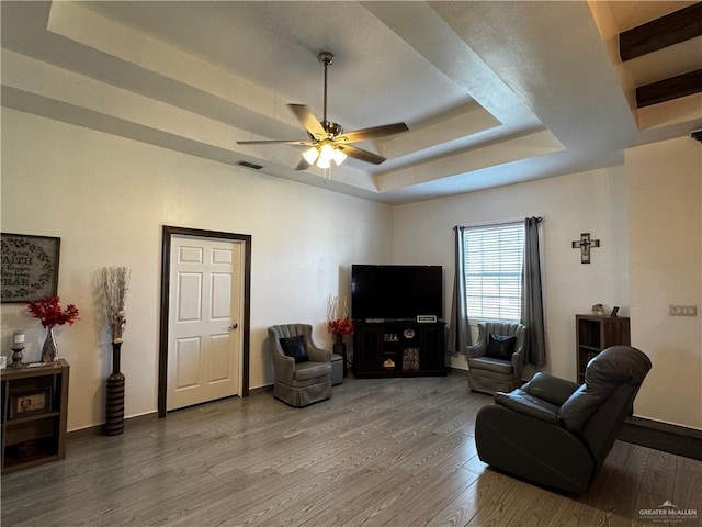 living room featuring wood-type flooring, a tray ceiling, and ceiling fan