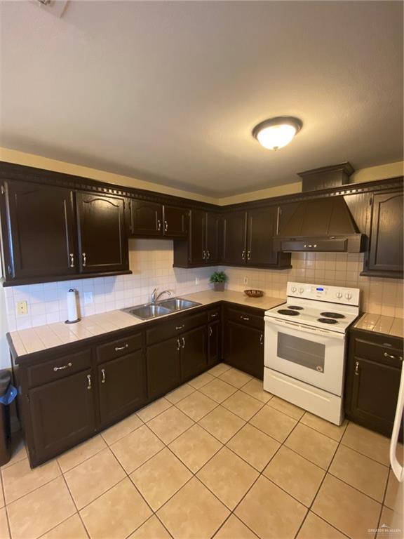 1903 E Llano Grande St, Weslaco, TX 78596 - kitchen with white range with electric cooktop, a sink, tile countertops, light tile patterned flooring, and backsplash
