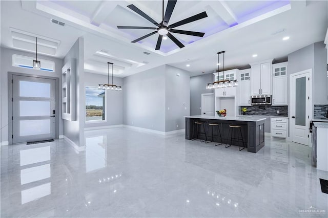 kitchen with coffered ceiling, a large island, white cabinets, and decorative light fixtures