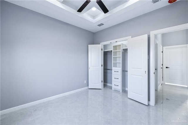 unfurnished bedroom with ceiling fan, a tray ceiling, a spacious closet, and a closet