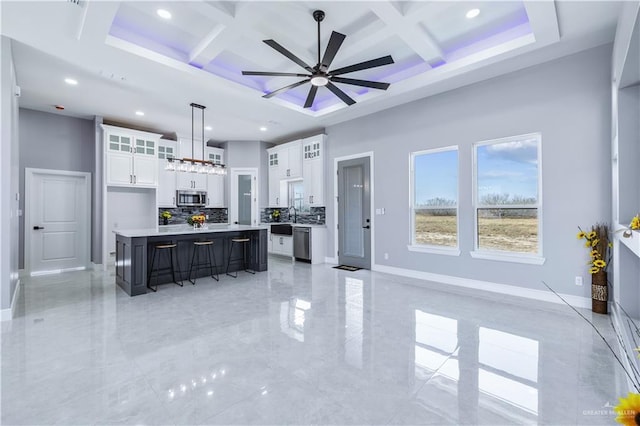 kitchen with appliances with stainless steel finishes, a towering ceiling, white cabinets, hanging light fixtures, and a center island