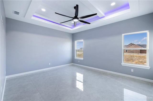 empty room with ceiling fan and a raised ceiling