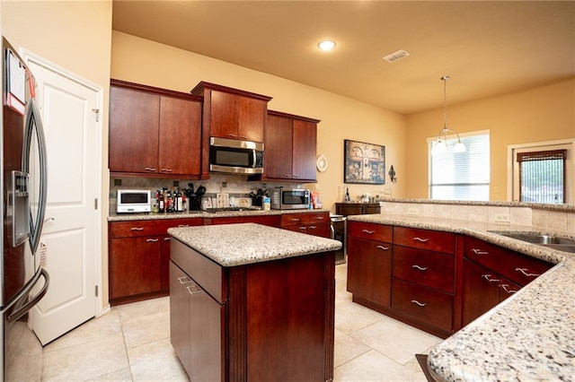 kitchen with light stone countertops, appliances with stainless steel finishes, a kitchen island, and pendant lighting